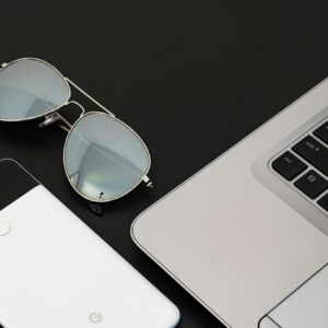A sleek flat lay of a laptop, smartphone, and sunglasses on a black surface.