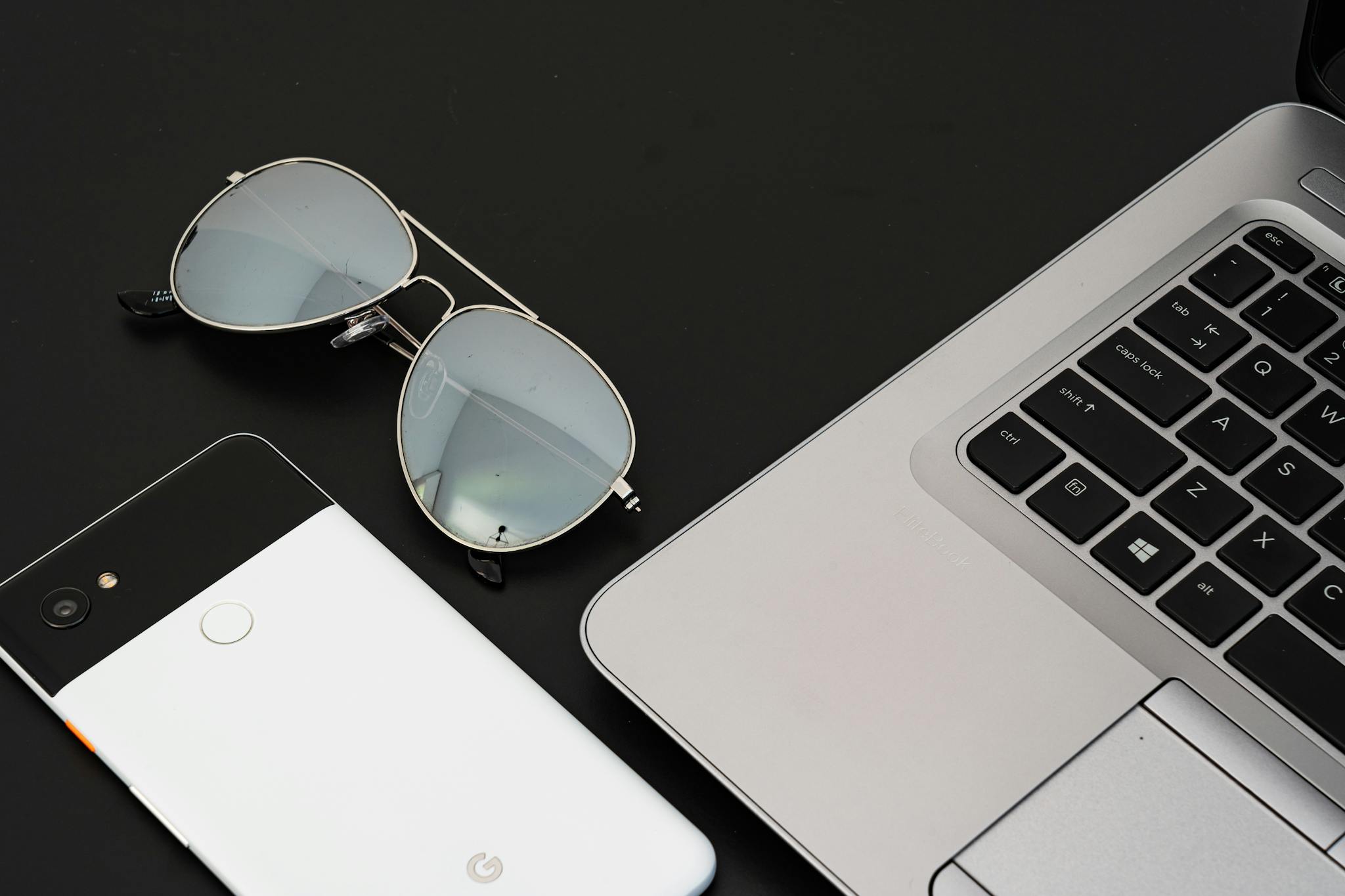 A sleek flat lay of a laptop, smartphone, and sunglasses on a black surface.
