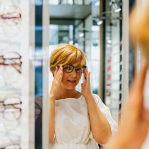 Adult woman trying on eyeglasses at an optical store, looking in a mirror.