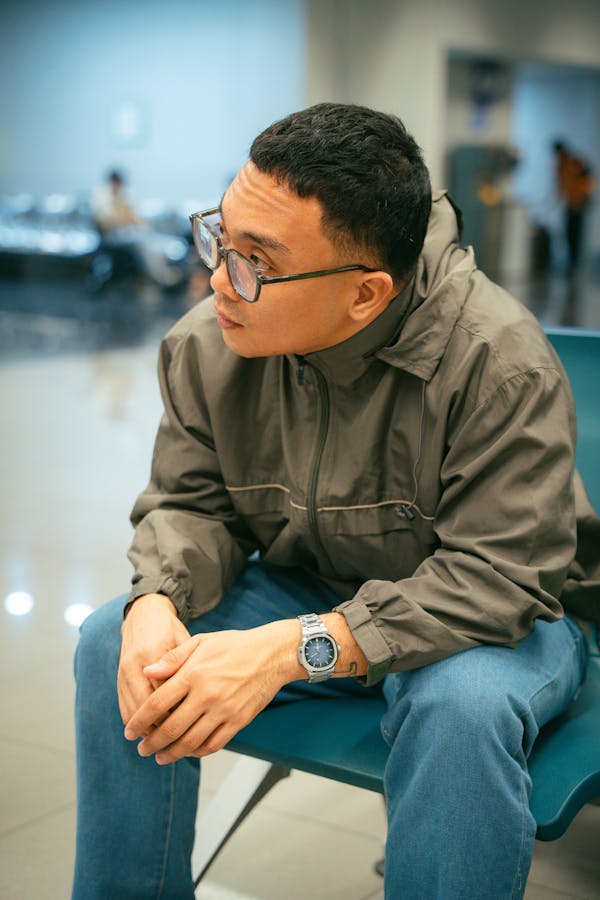 Casual portrait of a man sitting indoors, deep in thought, wearing glasses and a casual outfit.