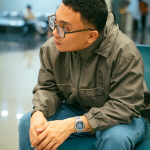 Casual portrait of a man sitting indoors, deep in thought, wearing glasses and a casual outfit.