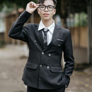 Confident young man in a tailored suit adjusting his glasses in an outdoor setting.