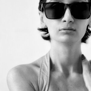 Monochrome portrait of a woman wearing fashionable sunglasses and a stylish top.
